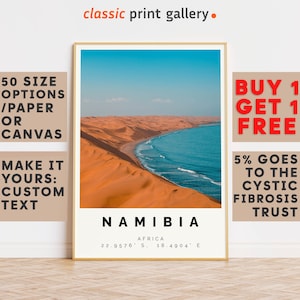 May include: A framed print showcasing the Namibian coastline, where golden sand dunes meet the turquoise ocean under a clear blue sky. The print includes the country's name, coordinates, and the text "classic print gallery."