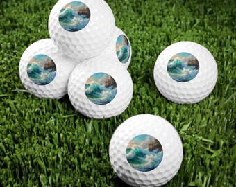 May include: Five white golf balls with a blue and green ocean wave painting on each ball. The golf balls are on a green grassy surface.