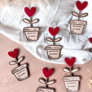 Peut inclure: Décorations florales en forme de cœur en bois avec des cœurs rouges et les noms Léa, Julie, Stéphanie, Laétitia, Clara et Marina. Chaque fleur porte un message en français. Les fleurs sont dans un pot.