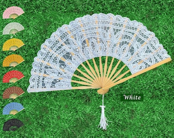 May include: White lace folding fan with a wooden handle and a white tassel. The fan is on a green grassy surface. DreamRoseStudio.etsy.com DreamRoseEvents.com