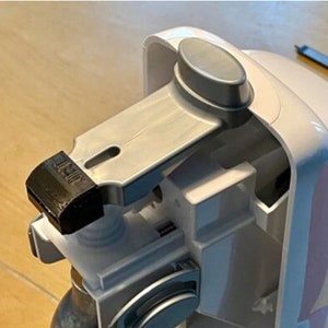 May include: A white and silver carbonation machine with a silver lever and a CO2 cartridge inserted. The cartridge is labeled "SodaStream CO2 Carbonating Cylinder".