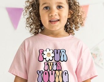 May include: A light pink t-shirt with the words "FOUR EVER YOUNG" in a colorful, retro font. The word "FOUR" features a smiling flower graphic. The shirt is short-sleeved and appears to be made of soft material.