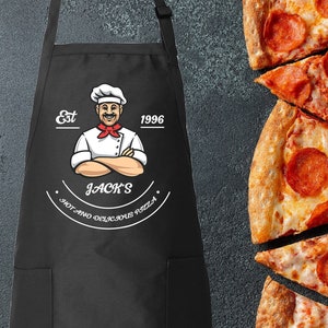 May include: Black apron with a white logo featuring a cartoon chef with the text "Est 1996 Jack's Hot and Delicious Pizza".