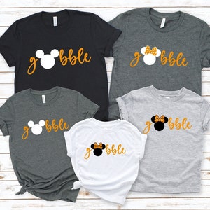 Peut inclure: Quatre t-shirts avec une t&ecirc;te de Mickey Mouse et le mot "gobble" imprim&eacute; dessus. Les t-shirts sont de diff&eacute;rentes couleurs&nbsp;: noir, gris, blanc et gris clair. Les t&ecirc;tes de Mickey Mouse sont de diff&eacute;rentes couleurs&nbsp;: blanc, noir et blanc avec des pois orange.