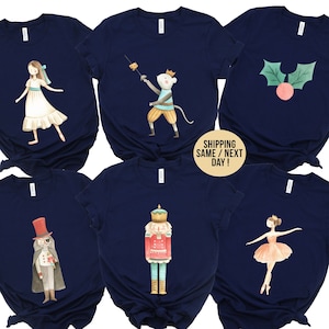 May include: Set of six navy blue t-shirts with different watercolor illustrations of characters from the Nutcracker ballet. The illustrations include a ballerina, a nutcracker soldier, a mouse king, a sugar plum fairy, and a Christmas tree.