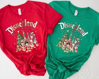 Puede incluir: Dos camisetas de manga corta, una roja y otra verde, con un diseño de Disneyland. El diseño incluye el logotipo de Disneyland, un árbol de Navidad y varios personajes de dibujos animados. Las camisetas son de material suave.