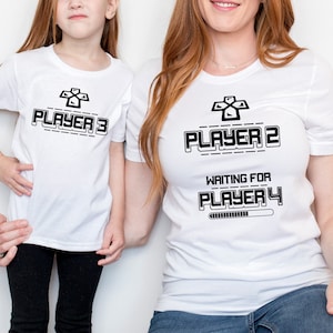 May include: Two white t-shirts with black text and a game controller graphic. The larger shirt says "Player 2 Waiting for Player 4" with a progress bar. The smaller shirt says "Player 3".