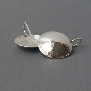 May include: A pair of silver earrings with a hammered, round disc design. The earrings have a simple wire hook fastening.