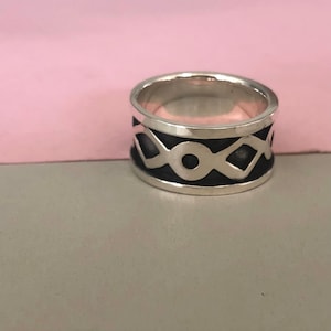 May include: A silver ring with a black geometric design. The ring is wide and has a rounded band.