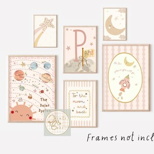 May include: A collection of framed art prints with a celestial theme. The prints feature illustrations of planets, stars, moons, and the text "The Solar System" and "To the moon and back". The color palette includes pink, beige, and gold.