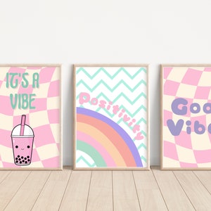 May include: Three framed prints with pink and white checkered backgrounds. The left print features a pink bubble tea with a green straw and the text "It's a Vibe". The middle print features a rainbow with a green, blue, and purple background and the text "Positivity". The right print features the text "Good Vibes" in purple.