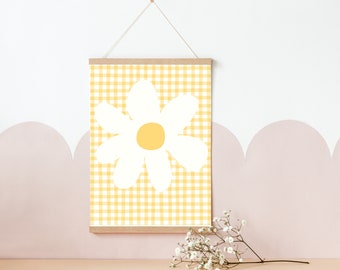 May include: A yellow and white gingham print with a white daisy in the center. The print is framed and hanging on a wall.