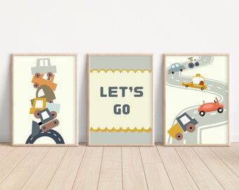 May include: Three framed prints with a yellow, gray, and white background. The left print features a stack of toy cars and trucks on a gray road. The middle print has the text "LET'S GO" in gray letters. The right print shows a yellow taxi, a red car, and a yellow construction vehicle driving on a gray road.