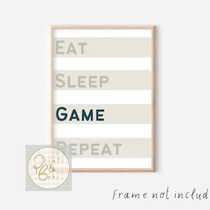 May include: A framed print featuring the words "EAT SLEEP GAME REPEAT" in a striped pattern. The word "GAME" is in dark teal, with the other words in light grey. The frame is a light wood colour.