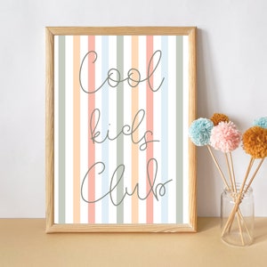 May include: A framed print with a striped background in shades of pink, blue, and green. The print features the text "Cool kids club" in a handwritten font.