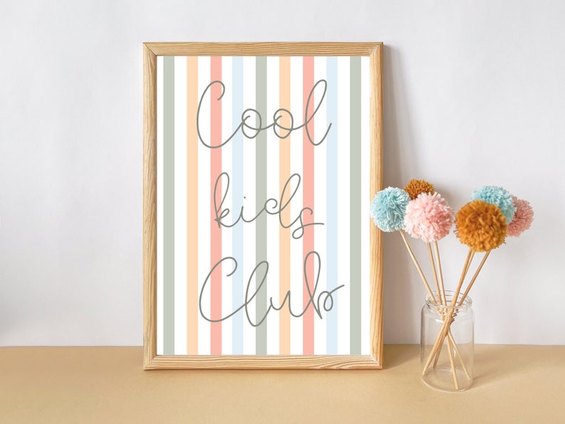 May include: A framed print with a striped background in shades of pink, blue, and green. The print features the text "Cool kids club" in a handwritten font.