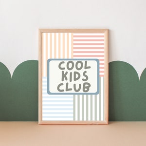 May include: A framed print with a striped background in shades of pink, orange, blue, and green. The print features a white rectangle with the text "COOL KIDS CLUB" in black.