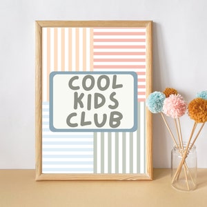 May include: A framed print with a striped pattern in peach, pink, blue, and gray. The print has the text "COOL KIDS CLUB" in a gray box.