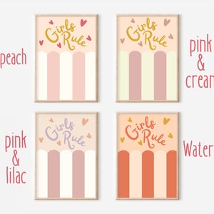 May include: Four printable wall art prints with the text "Girls Rule" in a gold script font. Each print features a different colour scheme: peach and cream, pink and cream, pink and lilac, and watermelon and cream. The prints have a striped pattern with rounded arches at the bottom.