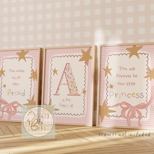 May include: Three framed prints with a pink and gold theme. Each print has a light pink background with a scalloped border and gold star accents. The prints feature text that reads "You make us so very Proud", "A is for Annie", and "You will forever be our little Princess".