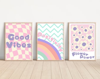 May include: Three pastel-colored prints with motivational messages. The first print has a pink and cream checkered background with the text "Good Vibes". The second print has a rainbow with a blue and green chevron background and the text "Positivity". The third print has a pink background with white flowers and the text "Flower Power".