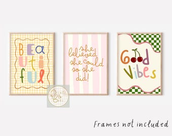 May include: Three framed art prints with inspirational quotes. The first print says "BEAUTIFUL" in colorful letters on a yellow gingham background. The second print says "She believed she could so she did!" on a pink striped background. The third print says "Good Vibes" with cherries.
