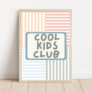May include: A framed print with a striped background in shades of pink, peach, blue, and gray. The print features a blue rectangle with the text "COOL KIDS CLUB" in gray.