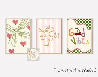May include: Set of three framed art prints. One features a bow and hearts, another has the text "She believed she could so she did!", and the third says "Good Vibes" with cherries. The prints have a light beige background.