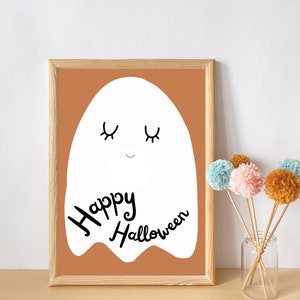 May include: A framed print with a white ghost illustration on a brown background. The ghost has closed eyes and a smile. The text "Happy Halloween" is written below the ghost.