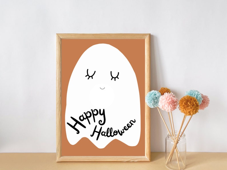 May include: A framed print with a white ghost illustration on a brown background. The ghost has closed eyes and a smile. The text "Happy Halloween" is written below the ghost.
