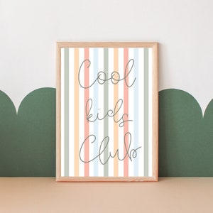 May include: A framed print with a striped background in shades of peach, light blue, and gray. The text "Cool kids club" is written in cursive on the print.