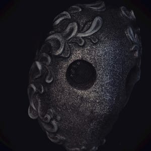 May include: A black masquerade mask with a silver glitter finish and intricate floral designs. The mask has a mesh eye opening.