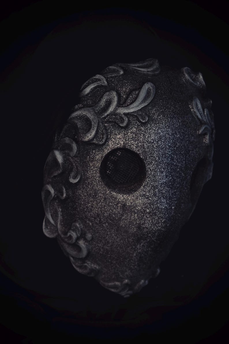 May include: A black masquerade mask with a silver glitter finish and intricate floral designs. The mask has a mesh eye opening.