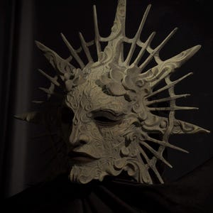 May include: A detailed, off-white mask with a sunburst design. The mask features intricate carvings and a serene facial expression. The mask is set against a dark background, highlighting its ornate details and texture.