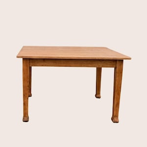 May include: A rectangular wooden table with a natural light brown finish and visible wood grain texture. The table features a flat top surface supported by four straight legs that taper slightly towards the bottom, providing a stable base.
