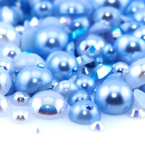 May include: A close-up of a pile of light blue iridescent pearls. The pearls are scattered on a white surface.