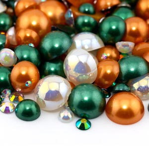 May include: A collection of round, iridescent, pearl-like beads in shades of white, green, and orange. The beads are scattered on a white surface.