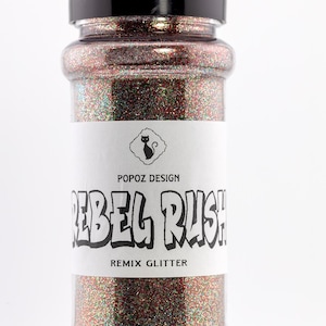 May include: A clear plastic jar filled with glitter. The glitter is a mix of red, green, and gold. The label reads "REBEL RUSH! REMIX GLITTER" with the Popoz Design logo of a cat.