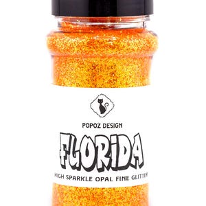 May include: A clear plastic shaker bottle filled with vibrant orange fine glitter. The bottle has a black screw-top lid and a white label featuring a black cat icon, the text POPOZ DESIGN, FLORIDA, and HIGH SPARKLE OPAL FINE GLITTER.