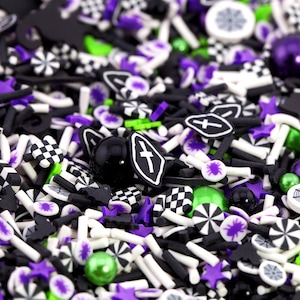May include: A close-up of a mix of Halloween-themed sprinkles in black, white, purple, and green. The sprinkles include shapes like stars, bats, tombstones, and checkerboard squares. Some are round, and some are stick-shaped.