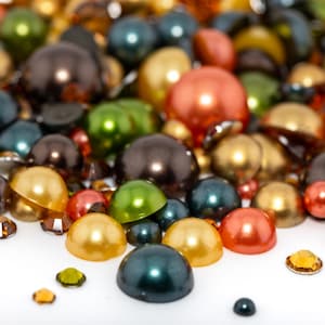 May include: A variety of colorful round beads in green, brown, gold, orange, and black. The beads are scattered on a white surface.