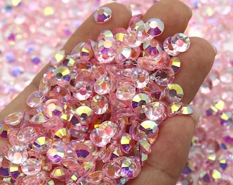 May include: A close-up of a hand holding a large amount of iridescent pink rhinestones. The rhinestones are scattered and overlapping, creating a shimmering effect.