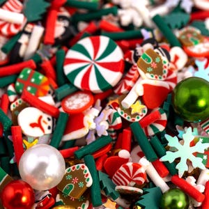 May include: A colorful assortment of Christmas-themed embellishments. The mix includes red and white peppermint candies, green Christmas trees, gingerbread men, snowmen, and snowflake shapes. There are also green and red beads and a large green ornament. The overall effect is festive and cheerful.