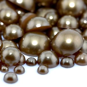May include: A pile of iridescent brown pearl-like beads of various sizes. The beads are scattered on a white surface.