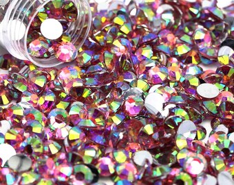Könnte beinhalten: Nahaufnahme einer großen Menge an regenbogenfarbenen rosa Strasssteinen. Die Strasssteine sind auf einer weißen Oberfläche verstreut und haben verschiedene Größen.