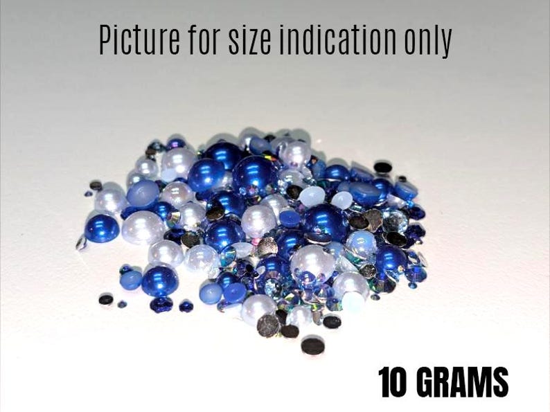 May include: A close-up of a pile of blue and white pearl-like beads and rhinestones. The beads are various sizes and shapes. The text "10 GRAMS" is visible at the bottom of the image.