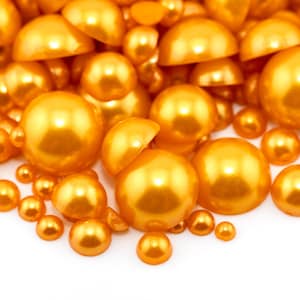 May include: A collection of golden, semi-spherical beads of varying sizes, scattered against a white background. The beads have a glossy, reflective surface, creating a warm, inviting aesthetic. Ideal for craft projects or decorative purposes.