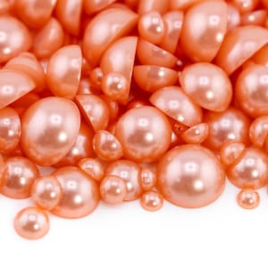 May include: Close-up of a collection of peach-colored, half-round, and full-round pearls. The pearls vary in size, with a glossy finish. The image is set against a white background, highlighting the texture and color of the beads.