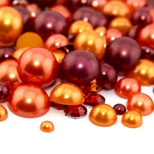 May include: A collection of pearl-like beads in shades of orange, red, and brown. The beads are scattered on a white surface.