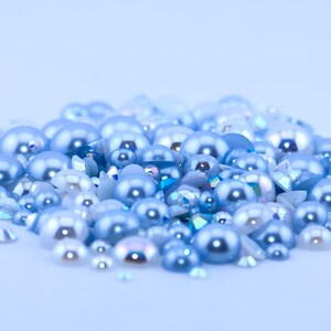 May include: A pile of light blue and white pearl-like beads and rhinestones. The beads are various sizes and shapes.